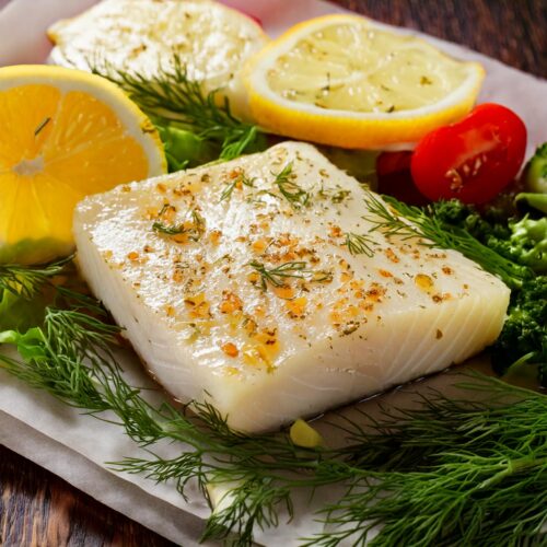 Firefly halibut filet up close with dill, lemon, pepper, butter and vegetables